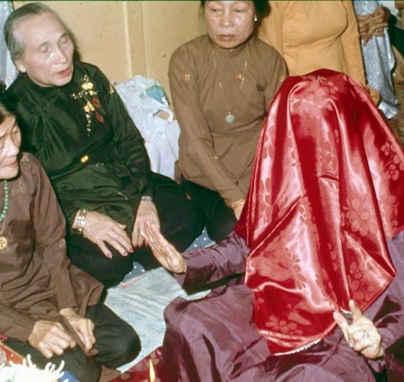 En prière et se cachant le visage sous le voile rouge de la prise de possession, la Ba Dong est tour à tour possédée par plusieurs Génies. Au second plan, on reconnaît Mmes Martin, Revue, Isnard. © Gluntz